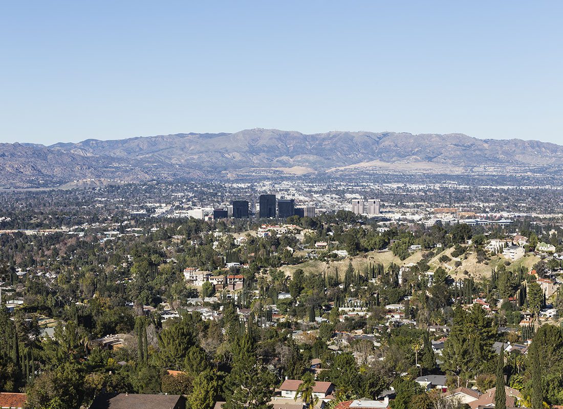 Contact - Aerial View of San Fernando Valley with Homes and Buildings Surrounded by Green Foliage with Mountains in the Background Against a Clear Blue Sky