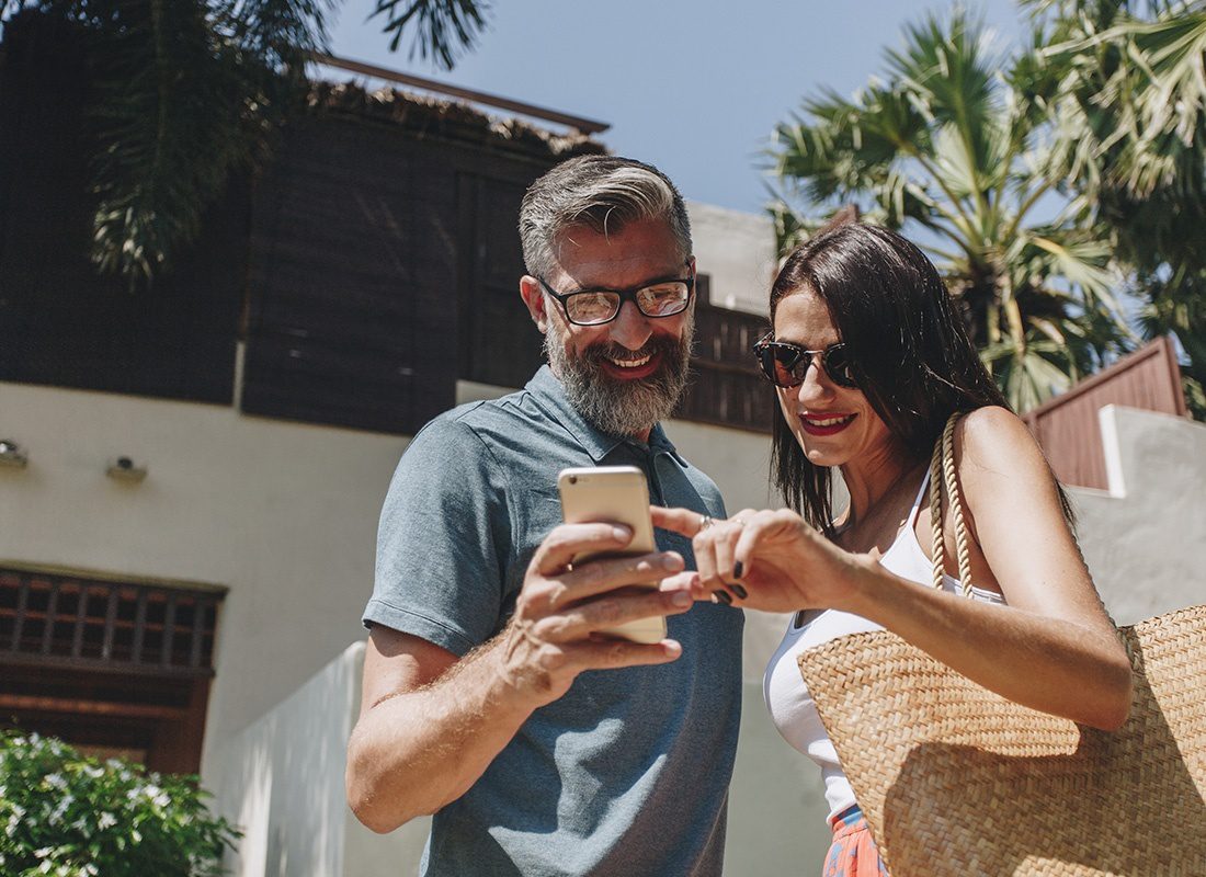 Read Our Reviews - Portrait of a Cheerful Mature Couple Standing Outside a Home in Sunny California While Using a Phone