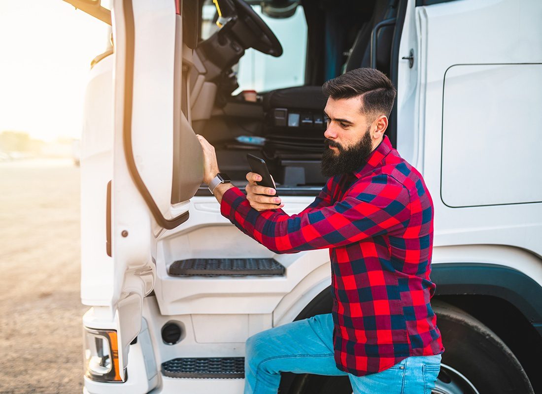 Service Center - Portrait of a Bearded Young Truck Driver Wearing a Plaid Shirt Standing Next to His Truck